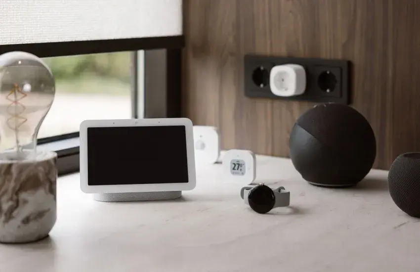 Google Nest Hub, Amazon Echo and HomePod mini on a desk beside a MotionBlinds roller blind, the smart home platforms MotionBlinds works with, supplied by Custom Blinds Shutters & Awnings