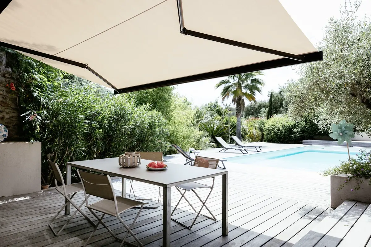 A Somfy motorised folding arm awning extended over a poolside dining deck, Somfy automation installed by Custom Blinds Shutters & Awnings