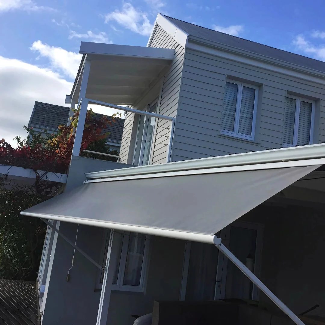 A grey fall-arm awning by Custom Blinds Shutters & Awnings extended over a doorway of a white weatherboard home, Thesen Island, Knysna, Garden Route, South Africa