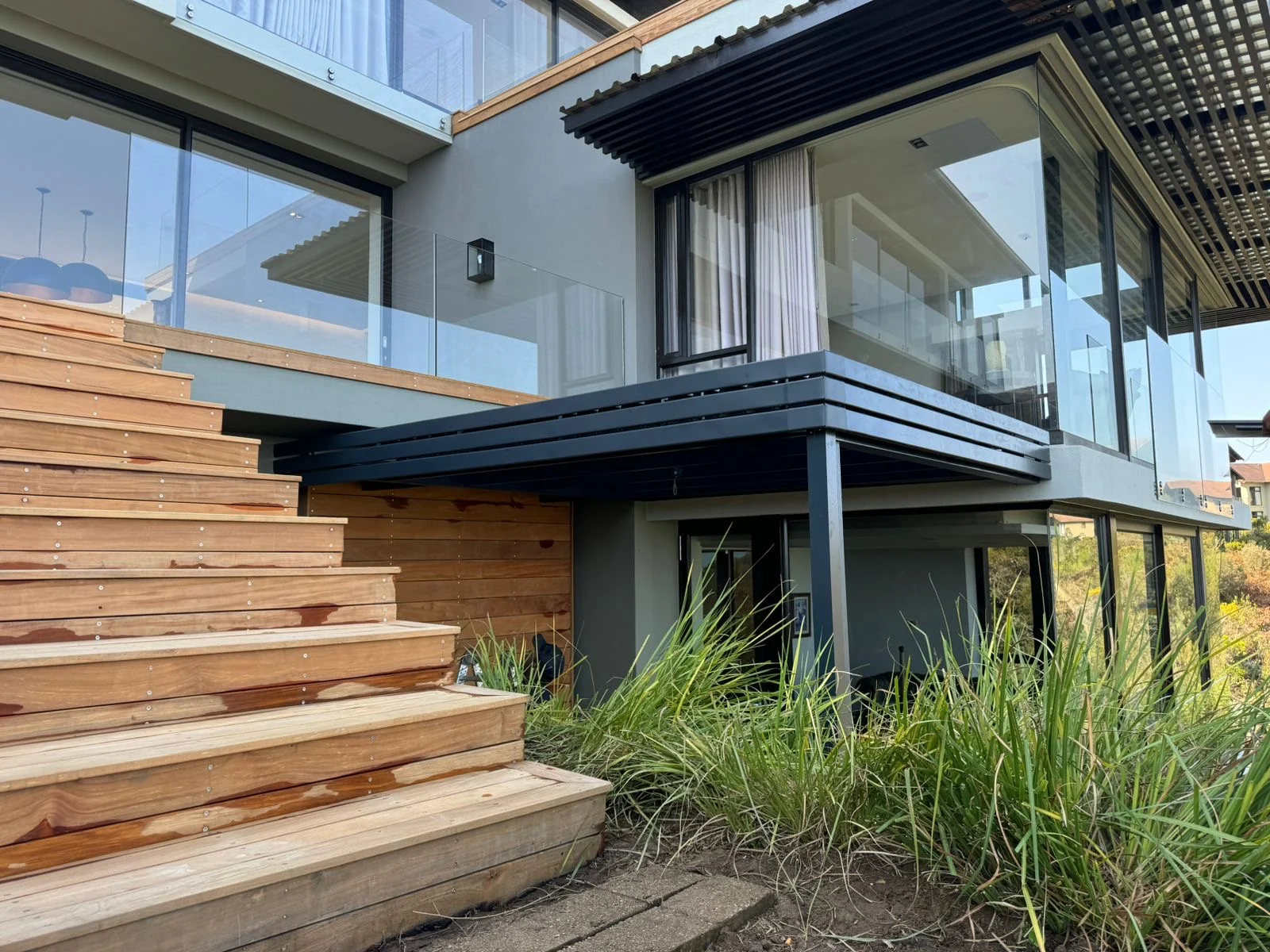 A charcoal louvre awning by Custom Blinds Shutters & Awnings as a canopy over a lower terrace beside timber stairs, Simola Golf Estate, Knysna, Garden Route, South Africa