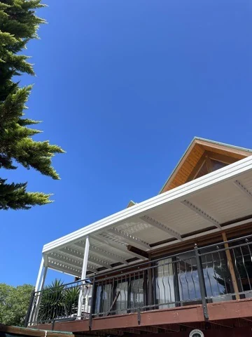 A white louvre awning by Custom Blinds Shutters & Awnings over a timber chalet balcony against a deep blue sky, Brenton-on-Sea, Knysna, Garden Route, South Africa