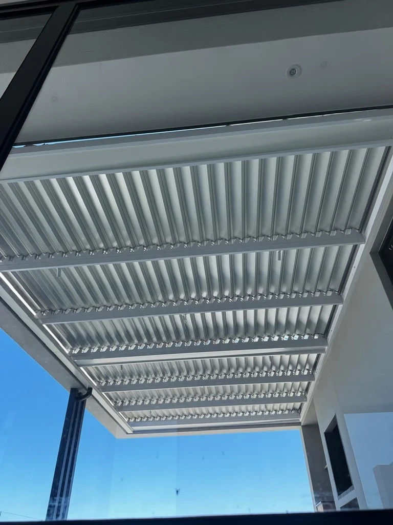 A white louvre awning by Custom Blinds Shutters & Awnings seen from inside through the glass, blades open to a blue sky, Fernwood Estate, Knysna, Garden Route, South Africa