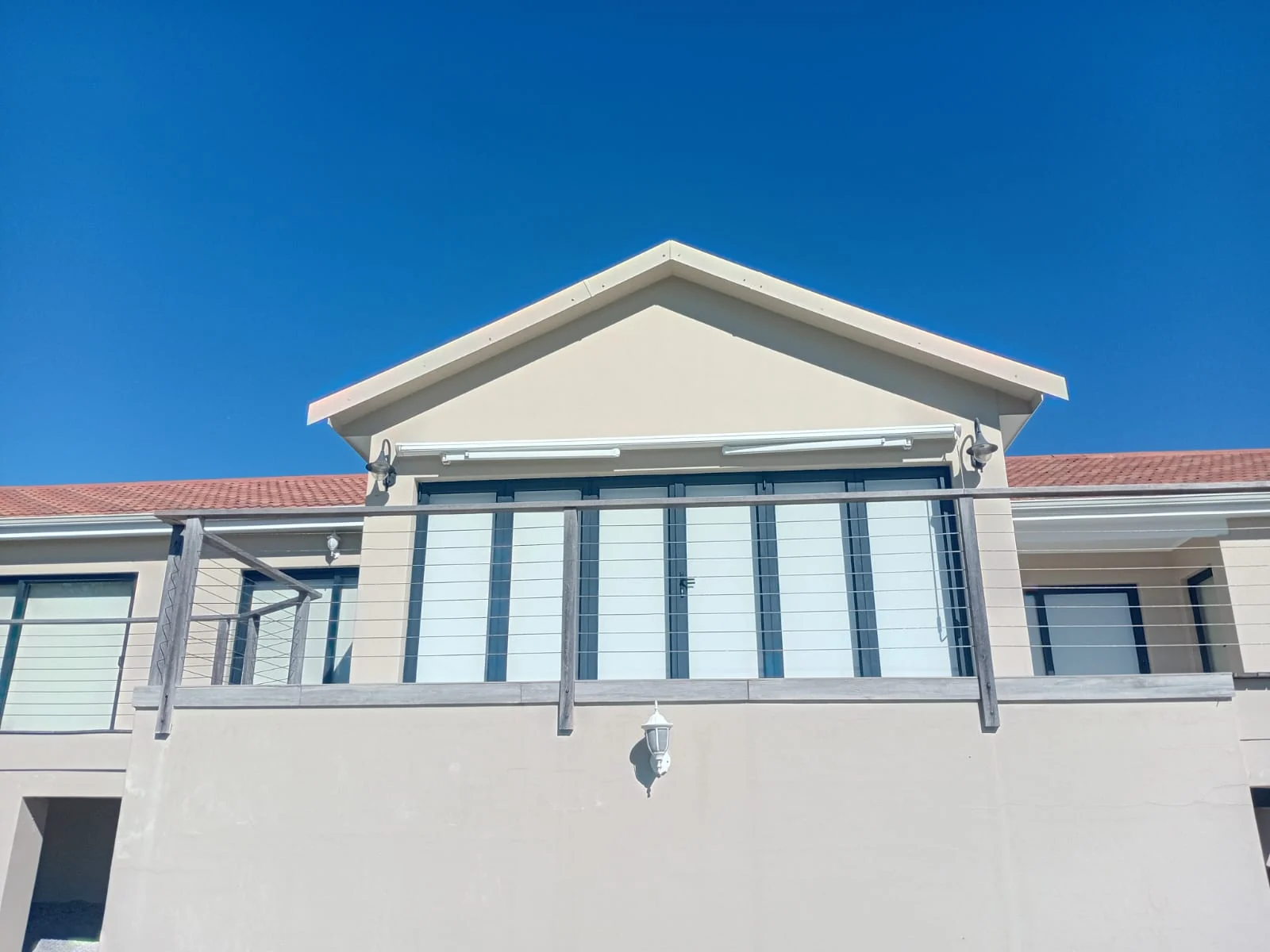A white retractable folding-arm awning by Custom Blinds Shutters & Awnings rolled back into its cassette under the gable, Plettenberg Bay, Garden Route, South Africa
