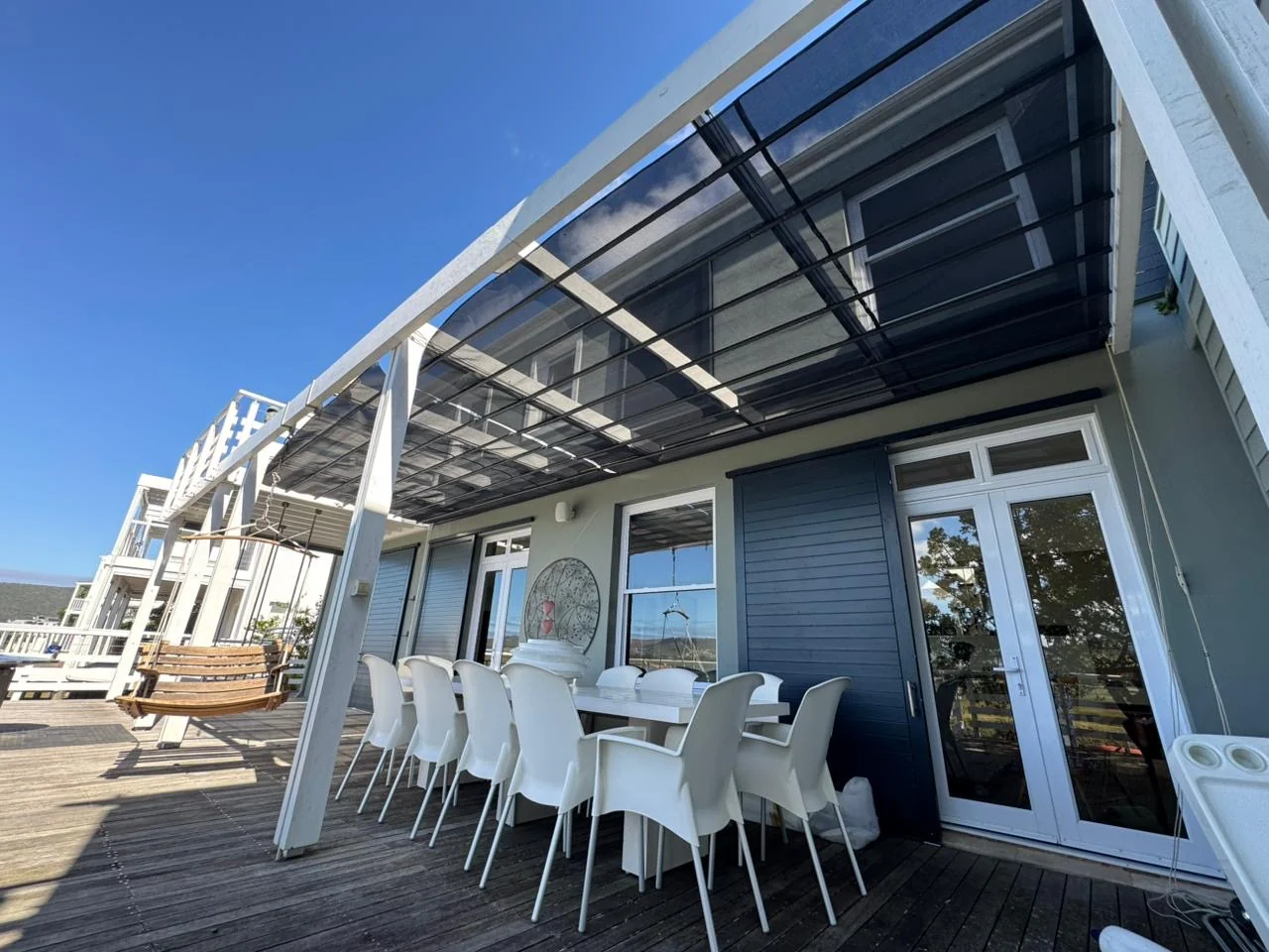 A custom-designed retractable patio shade awning by Custom Blinds Shutters & Awnings, black mesh along a white pergola over a timber deck, Thesen Island, Knysna, Garden Route, South Africa