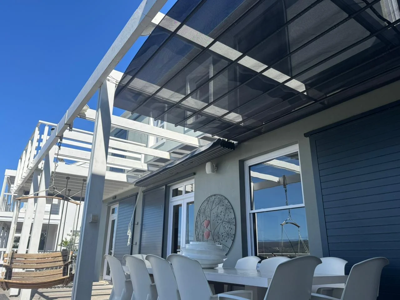 A custom-designed retractable patio shade awning by Custom Blinds Shutters & Awnings, black mesh drawn under a white pergola over an outdoor dining table, Thesen Island, Knysna, Garden Route, South Africa