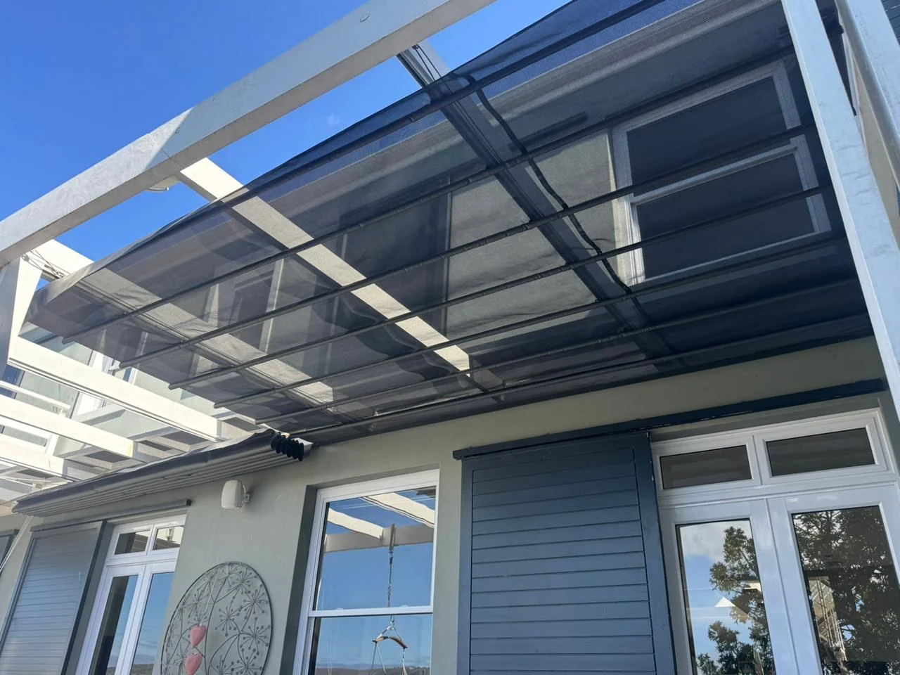 The underside of a custom-designed retractable patio shade awning by Custom Blinds Shutters & Awnings, black mesh on its guide bars beneath a white pergola, Thesen Island, Knysna, Garden Route, South Africa