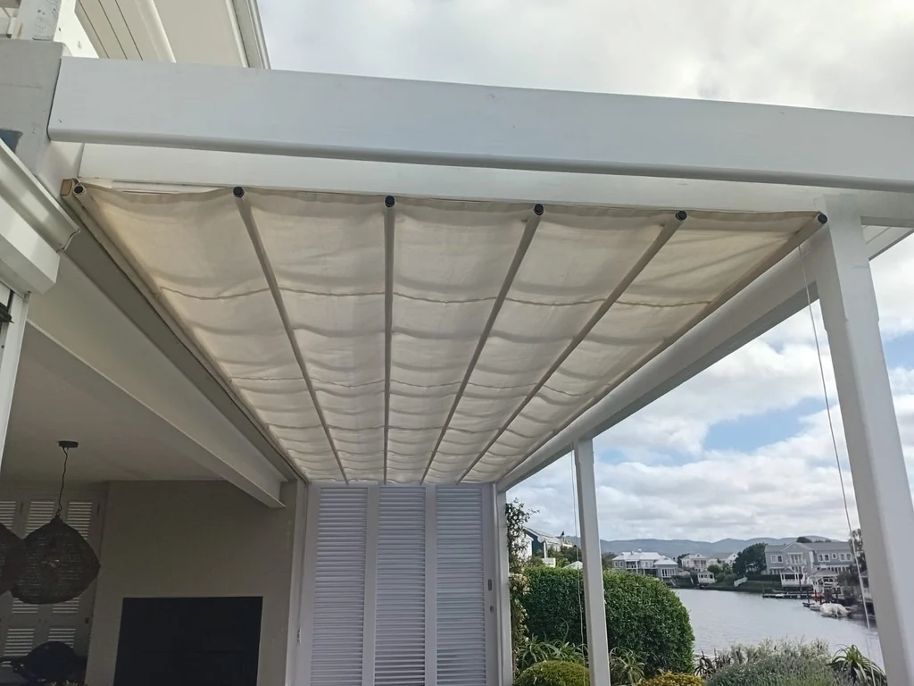 A cream canvas retractable patio shade awning by Custom Blinds Shutters & Awnings drawn along its wires under a white pergola, waterside homes beyond, Thesen Island, Knysna, Garden Route, South Africa
