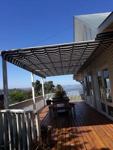 A grey and white striped canvas retractable patio shade awning by Custom Blinds Shutters & Awnings over a timber deck, the sea beyond, Westford Bridge, Knysna, Garden Route, South Africa