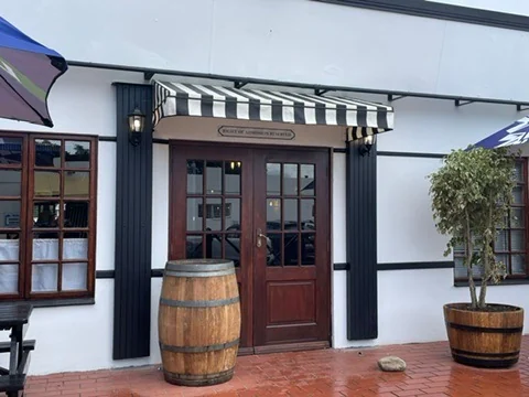 A black and white striped wedge awning by Custom Blinds Shutters & Awnings over the double doors of a restaurant, a barrel beside the entrance, Bosun's Pub, Knysna, Garden Route, South Africa