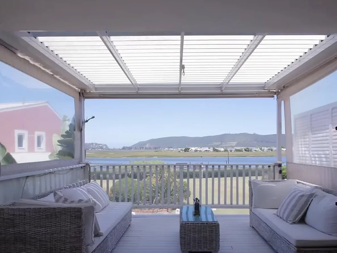 White louvred aluminium roof over a patio with clear side blinds and lagoon view, Custom Blinds Shutters & Awnings
