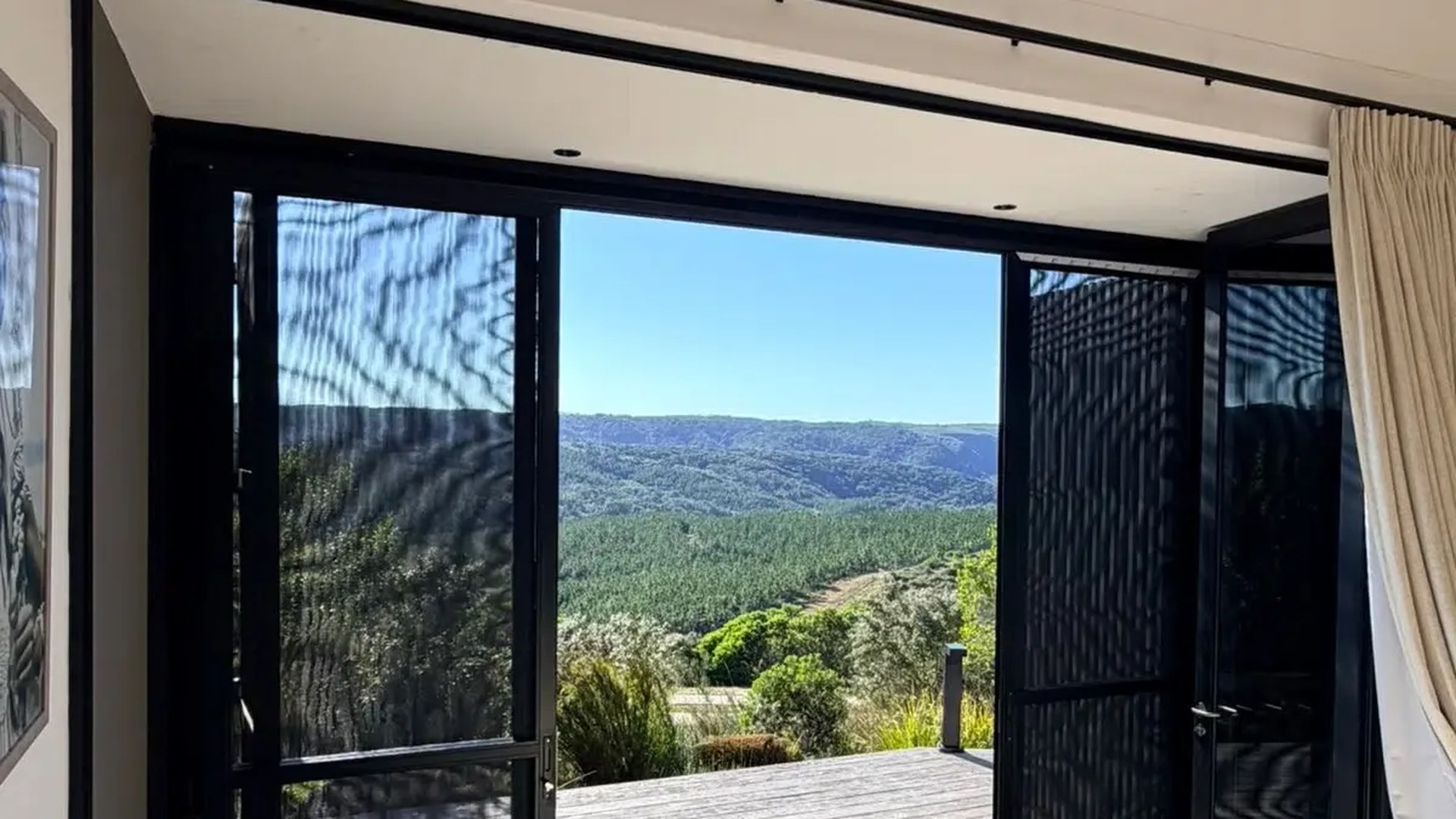 Open black-framed glass doors with a fine mesh fly screen panel and a forested valley view