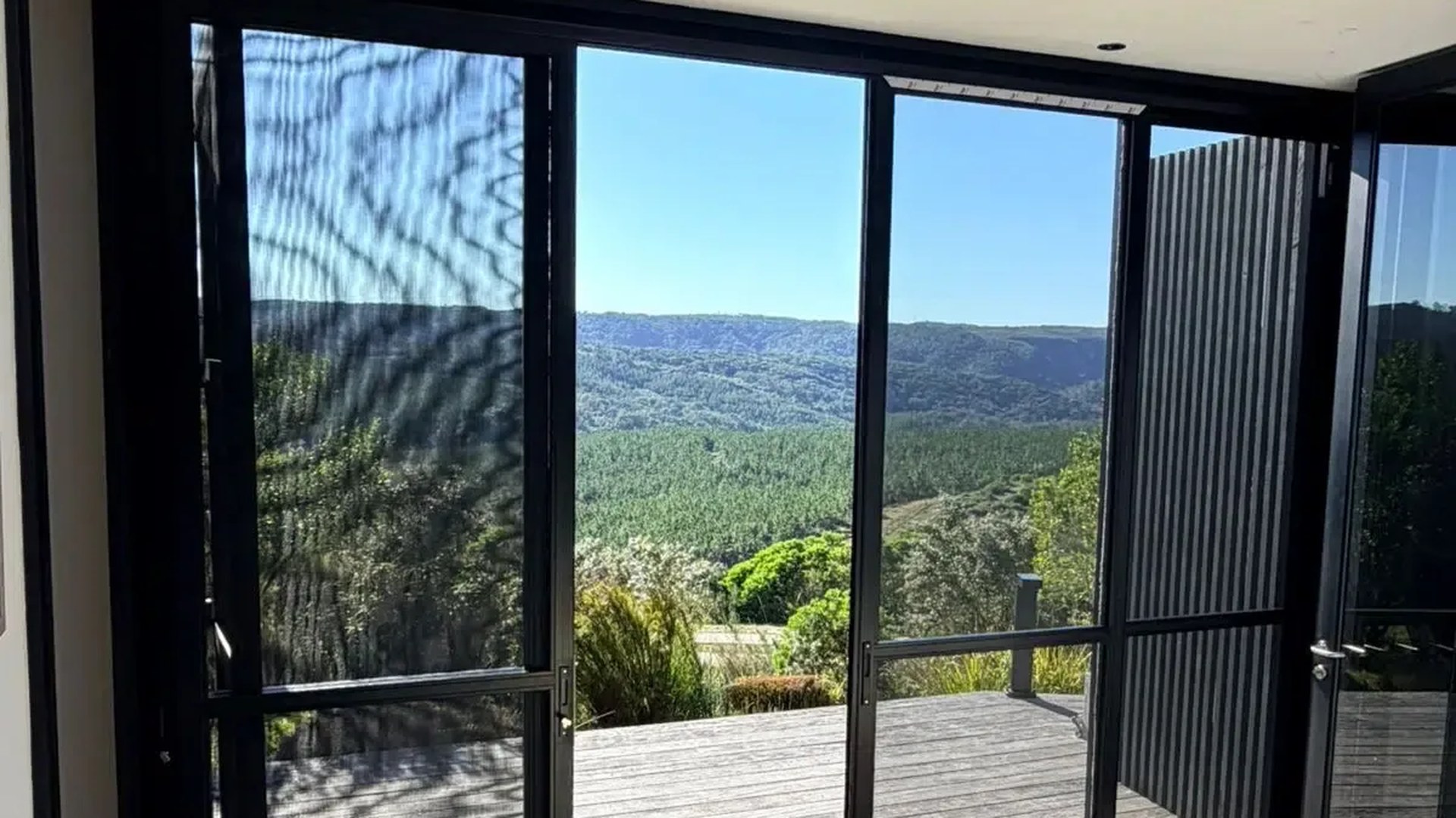 Black-framed glass doors with a fine mesh insect screen panel and a forested valley view