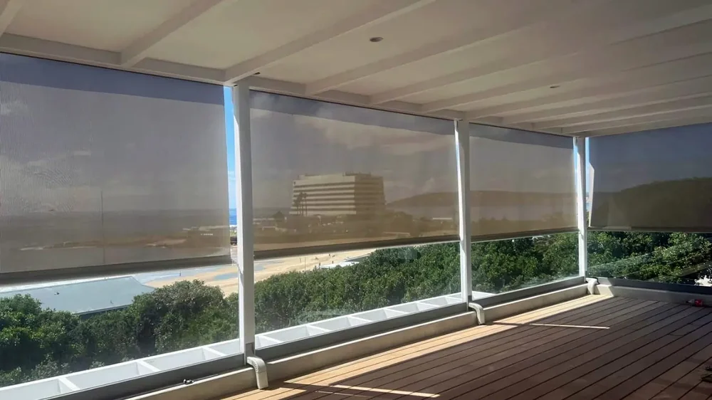 Sheer sunscreen outdoor blinds lowered across a covered deck with a sea view, installed by Custom Blinds Shutters & Awnings