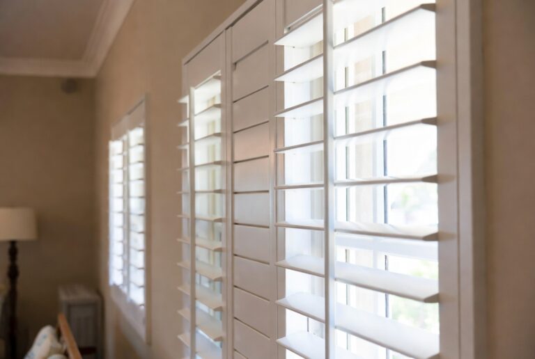 Full wall PVC indoor shutters in a Knysna apartment with lagoon light, white louvres open for ventilation, Custom Blinds Shutters & Awnings