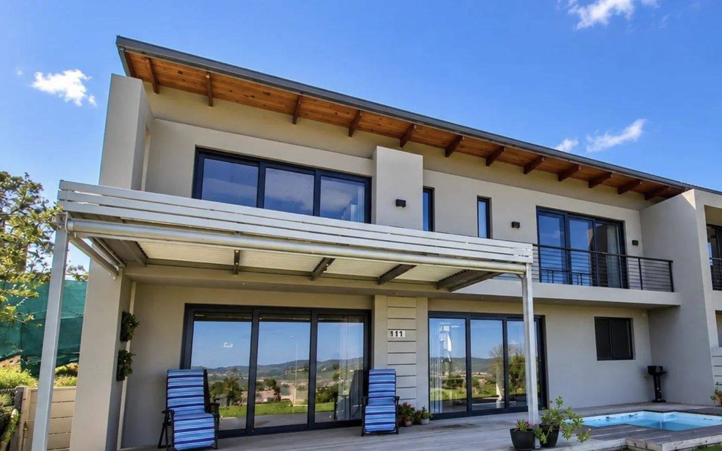 Aluminium louvred awning over a patio and pool deck at Simola Estate, Knysna, with outdoor blinds by Custom Blinds Shutters & Awnings
