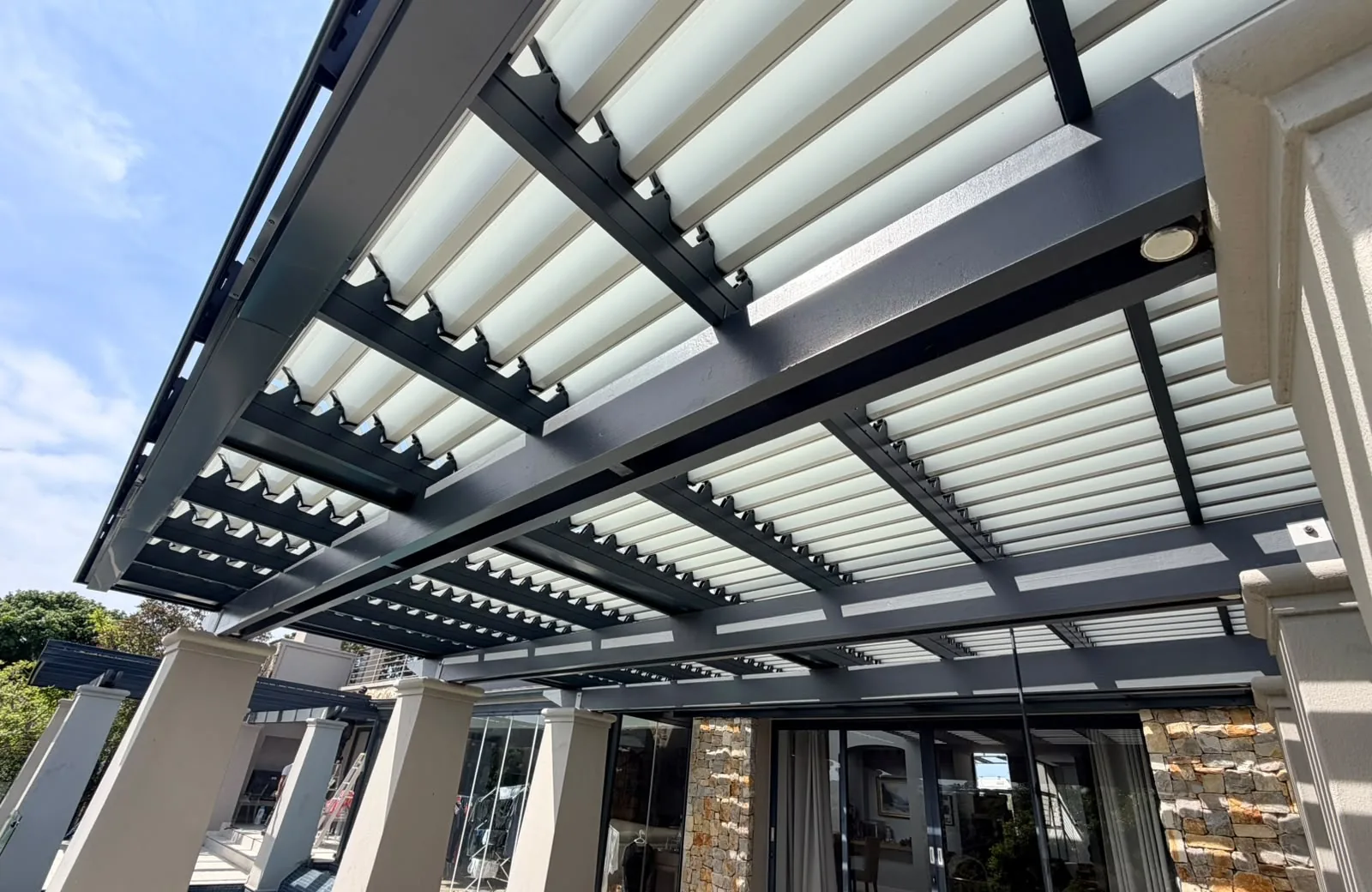 Charcoal aluminium louvred awning with white blades over a patio at Pezula Estate, Knysna, by Custom Blinds Shutters & Awnings