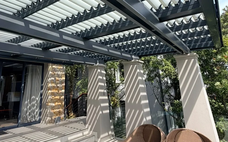 Aluminium louvred awning with blades open, casting striped shade across a patio at Pezula Estate, Knysna, by Custom Blinds Shutters & Awnings
