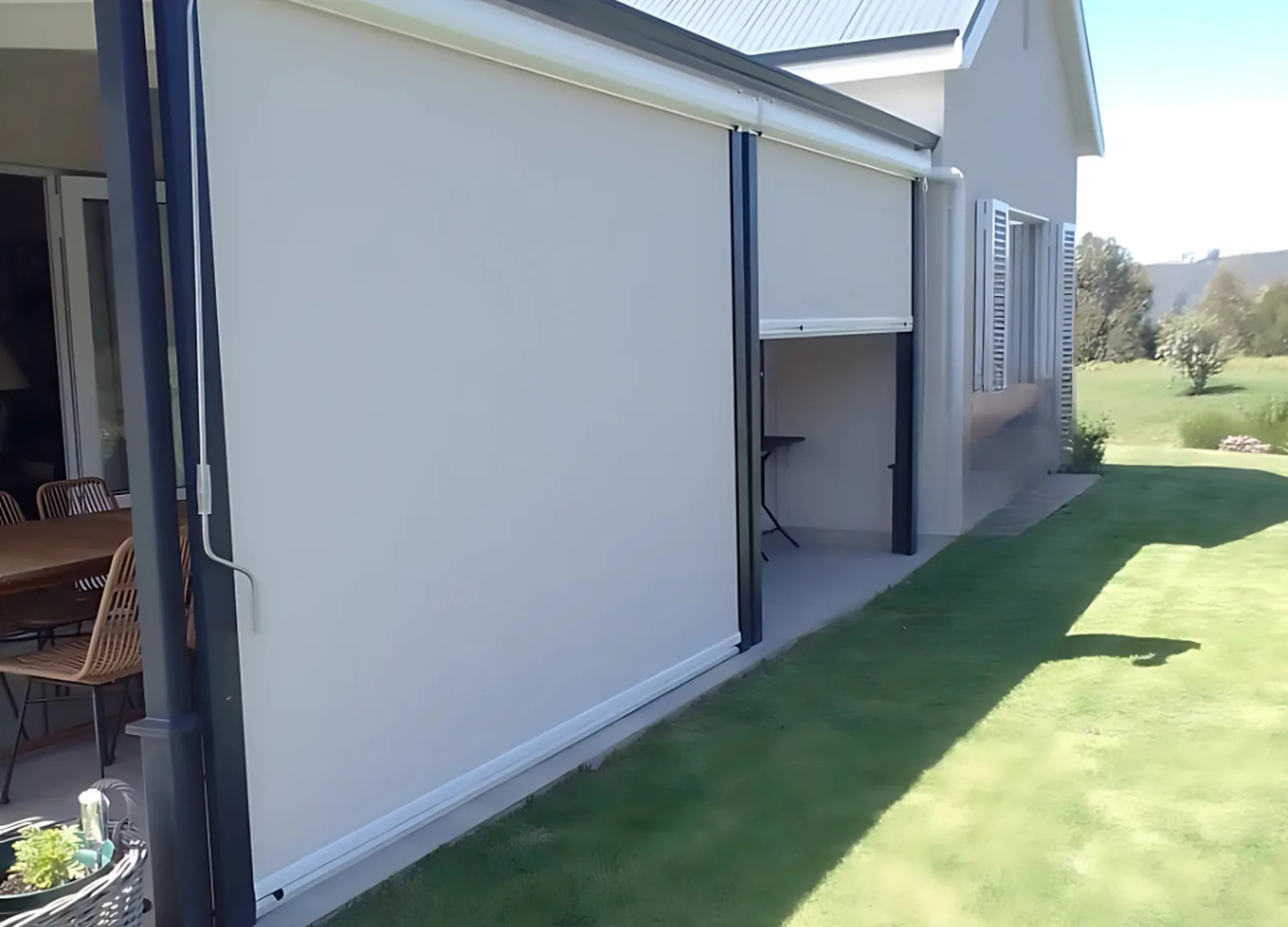 Screen mesh outdoor blinds running in side tracks down a covered veranda, charcoal guide tracks fixed to the posts, one bay left open, by Custom Blinds Shutters and Awnings