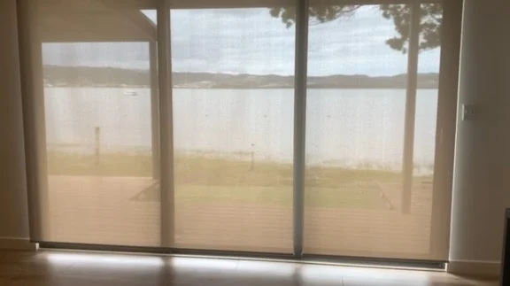 Automated roller blinds installed at Brenton-on-Lake, Knysna, by Custom Blinds Shutters & Awnings, sunscreen fabric lowered across sliding doors with the lagoon beyond