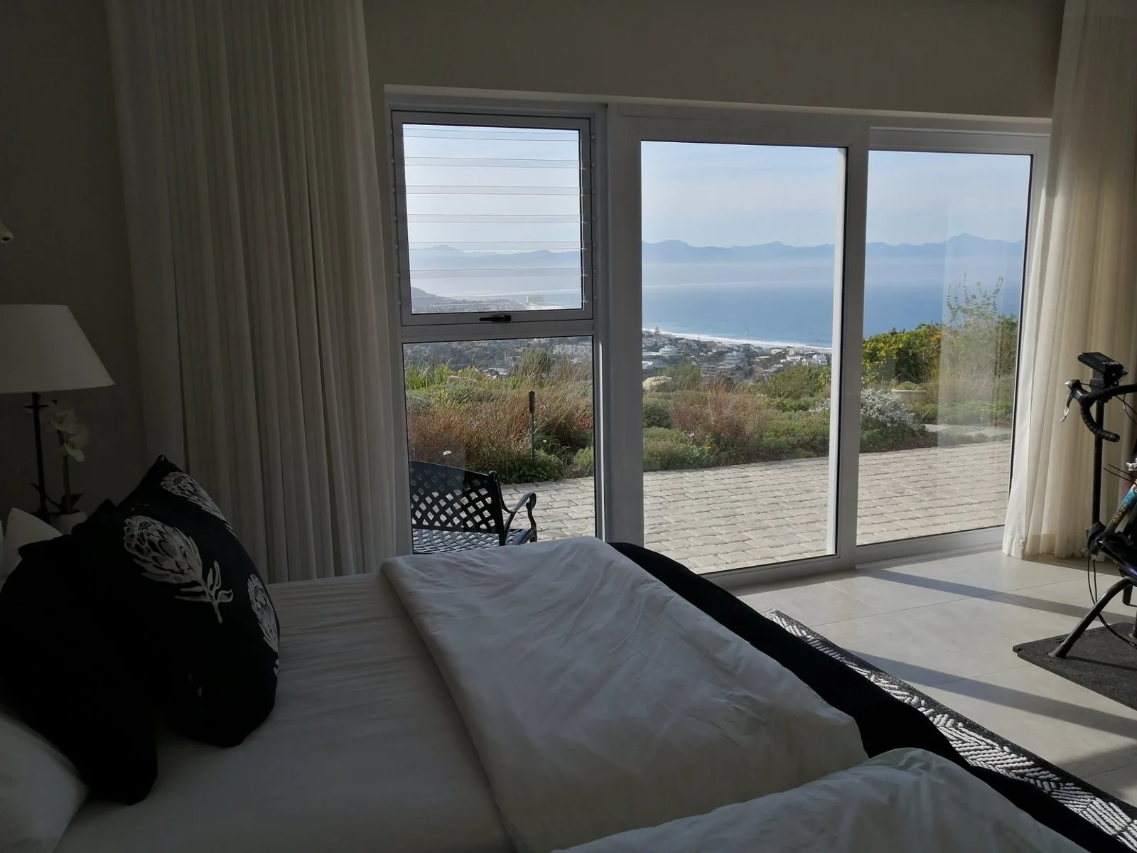 Bedroom with sliding glass doors opening to a paved patio and sea view, Custom Blinds Shutters & Awnings