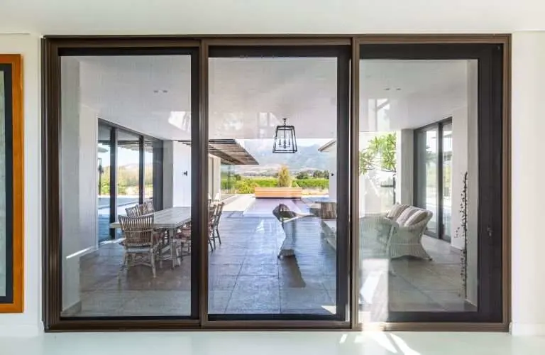 Bronze-framed sliding security screens across a three-panel opening to a patio with mountain views, by Custom Blinds Shutters & Awnings