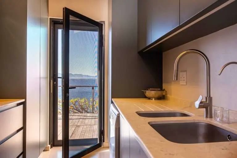 A black-framed security screen door open off a kitchen onto a deck with a sea view, by Custom Blinds Shutters & Awnings