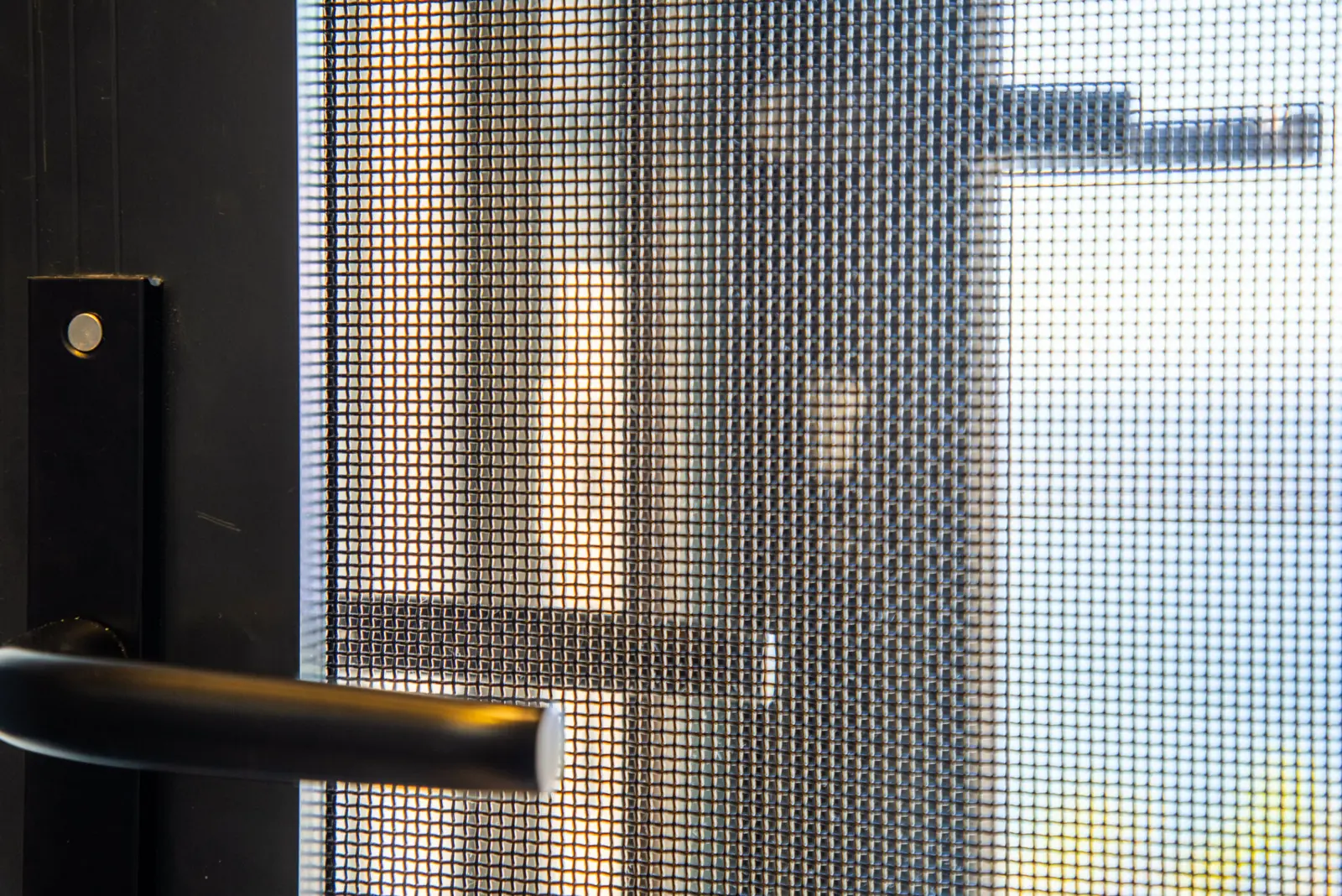 Close-up of woven stainless steel security mesh and a black handle on a screen door, by Custom Blinds Shutters & Awnings