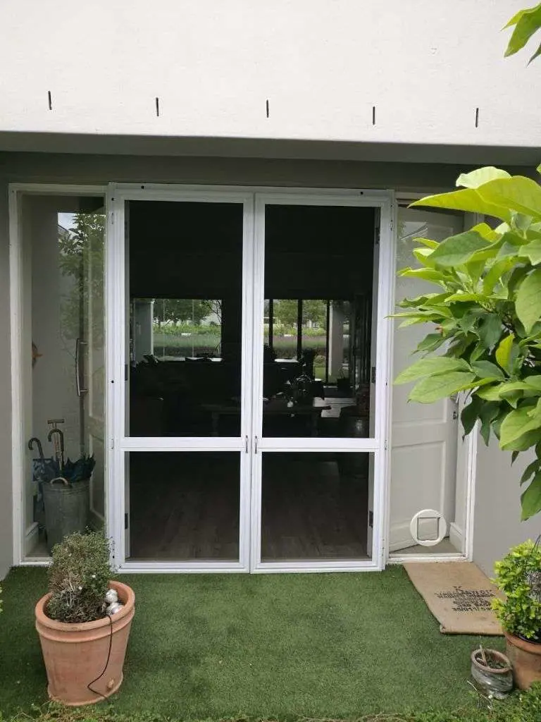 White double security screen doors closed on a garden courtyard, by Custom Blinds Shutters & Awnings