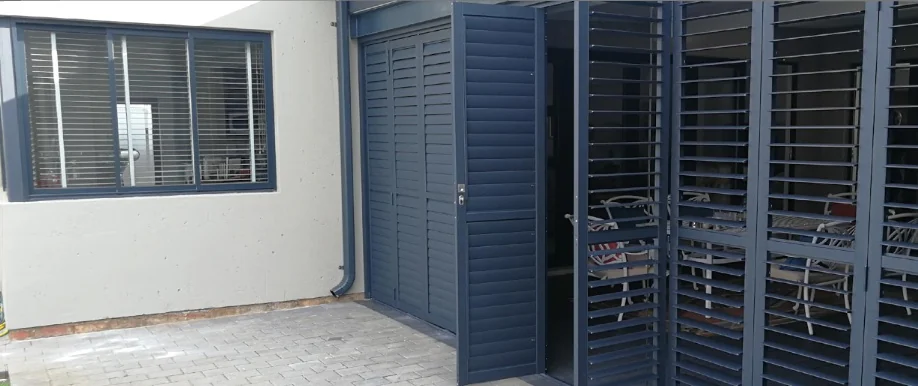 Charcoal aluminium security shutters by Custom Blinds Shutters & Awnings in a bi-fold run across an exterior opening, panels folded back