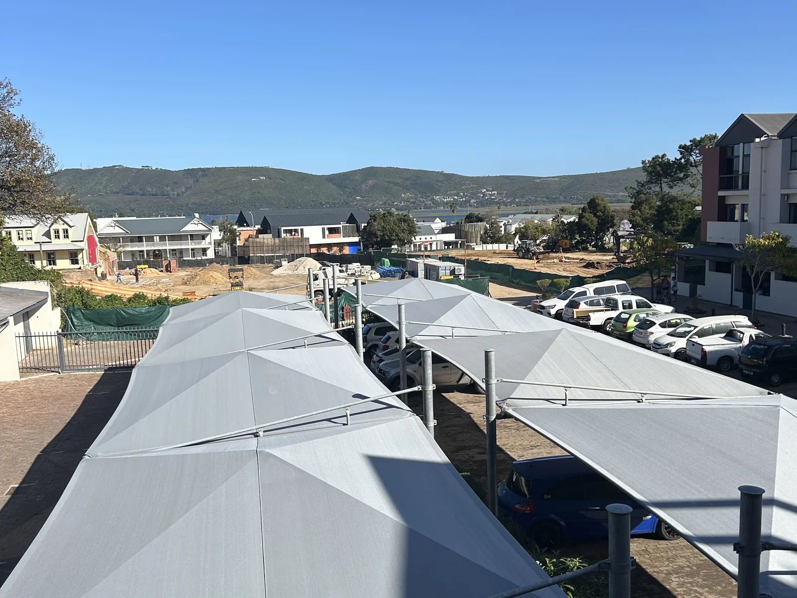 Grey multi bay shadeports by Custom Blinds Shutters & Awnings over the parking bays of a Knysna residential complex, the lagoon and the hills above Knysna beyond