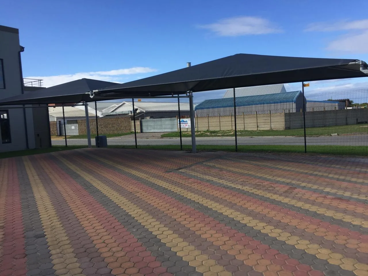 A charcoal multi bay shadeport installed by Custom Blinds Shutters & Awnings over a patterned brick parking area in Glentana, the shade cloth canopy running the length of the bays