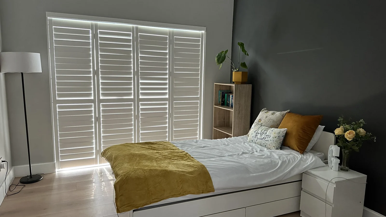 White PVC indoor shutters by Custom Blinds Shutters & Awnings across a wide bedroom window wall, louvres open
