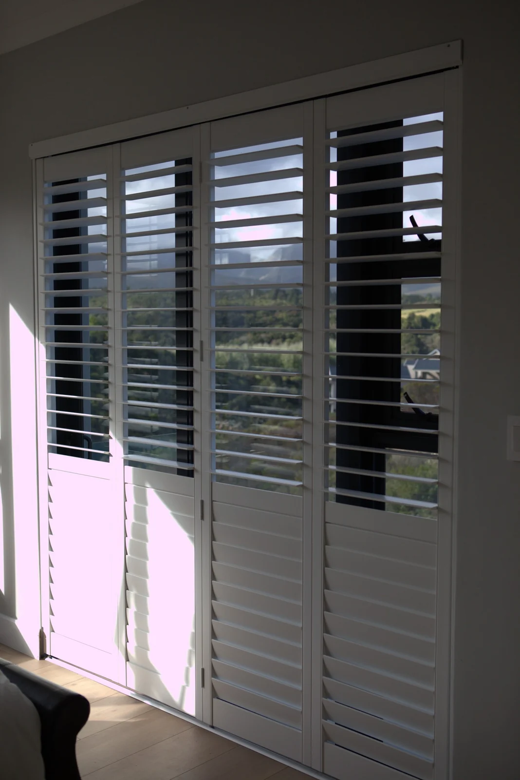 White bifold shutter panels across a corner window, blades half open, fitted by Custom Blinds Shutters & Awnings, George, Garden Route, South Africa