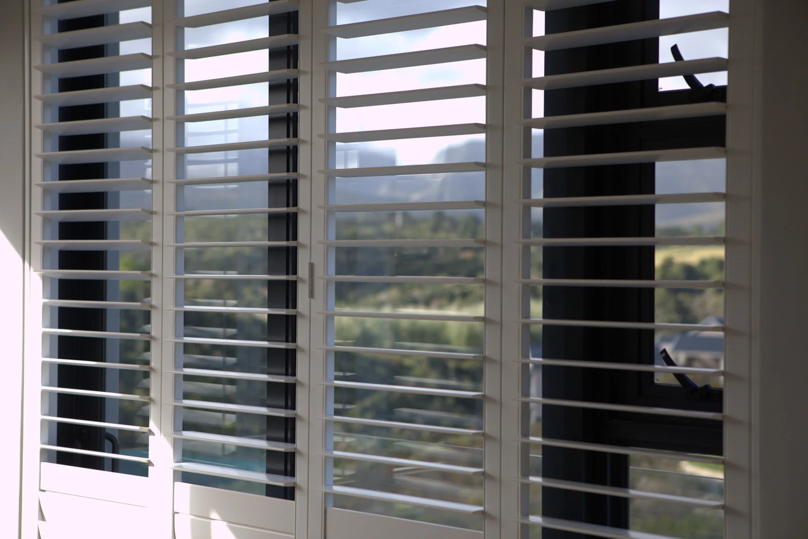White shutter blades tilted open to a hillside view, seen from inside, fitted by Custom Blinds Shutters & Awnings, George, Garden Route, South Africa