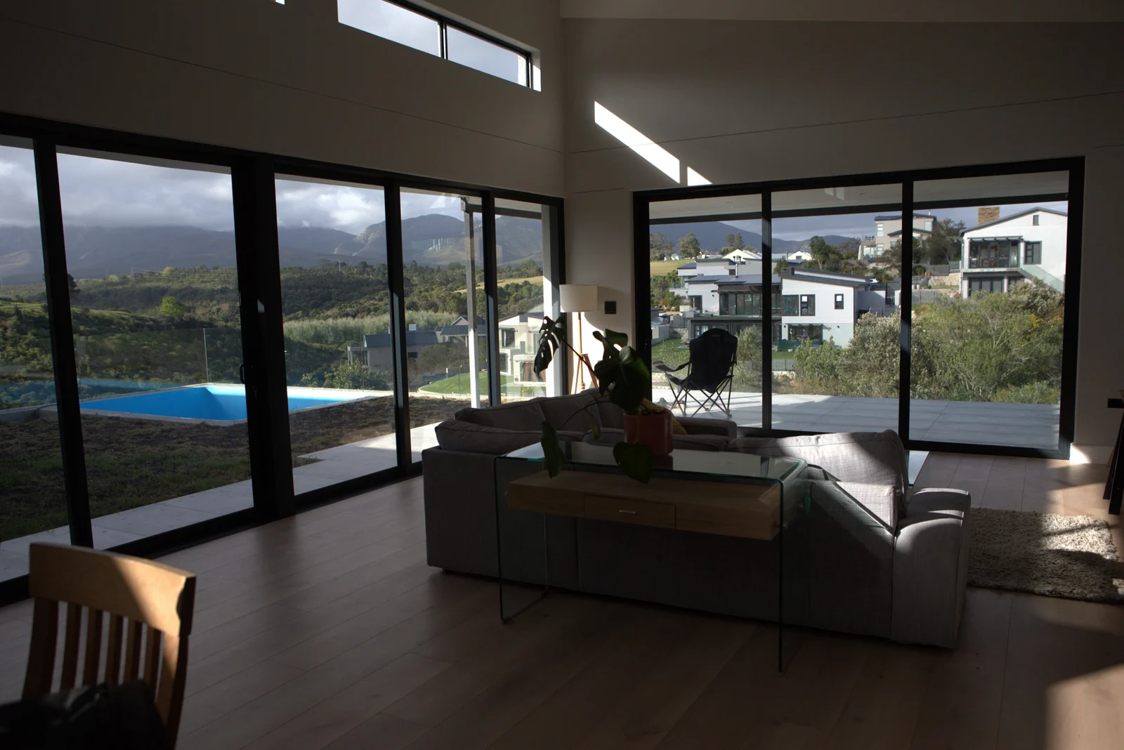 White indoor shutters folded back from an open-plan living room with a pool and hills beyond, fitted by Custom Blinds Shutters & Awnings, George, Garden Route, South Africa