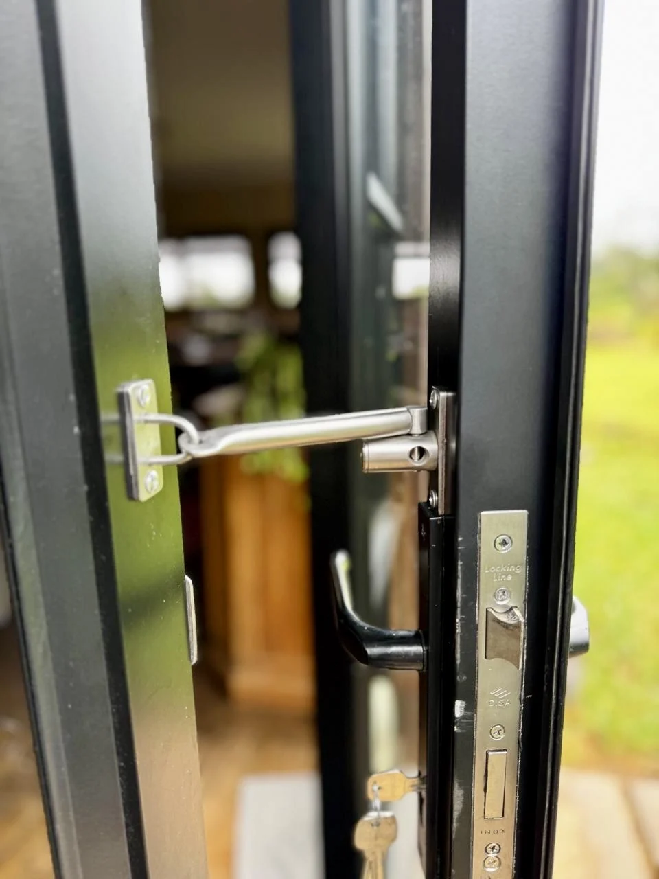 A black door, partly ajar with a secure latch, keeps your home safe whilst letting you enjoy fresh views of the garden and lounge. by Custom Blinds Shutters & Awnings, Garden Route, South Africa