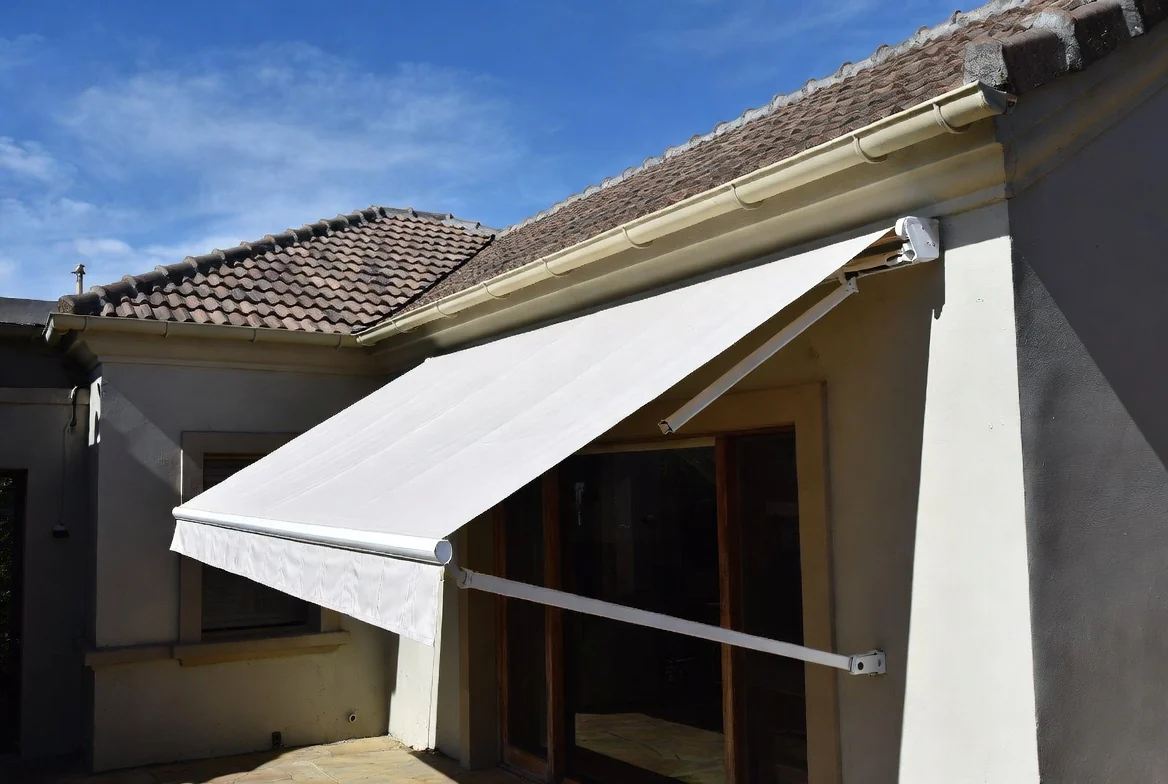 Fall arm awning in cream acrylic canvas over a window of a residential home by Custom Blinds Shutters & Awnings