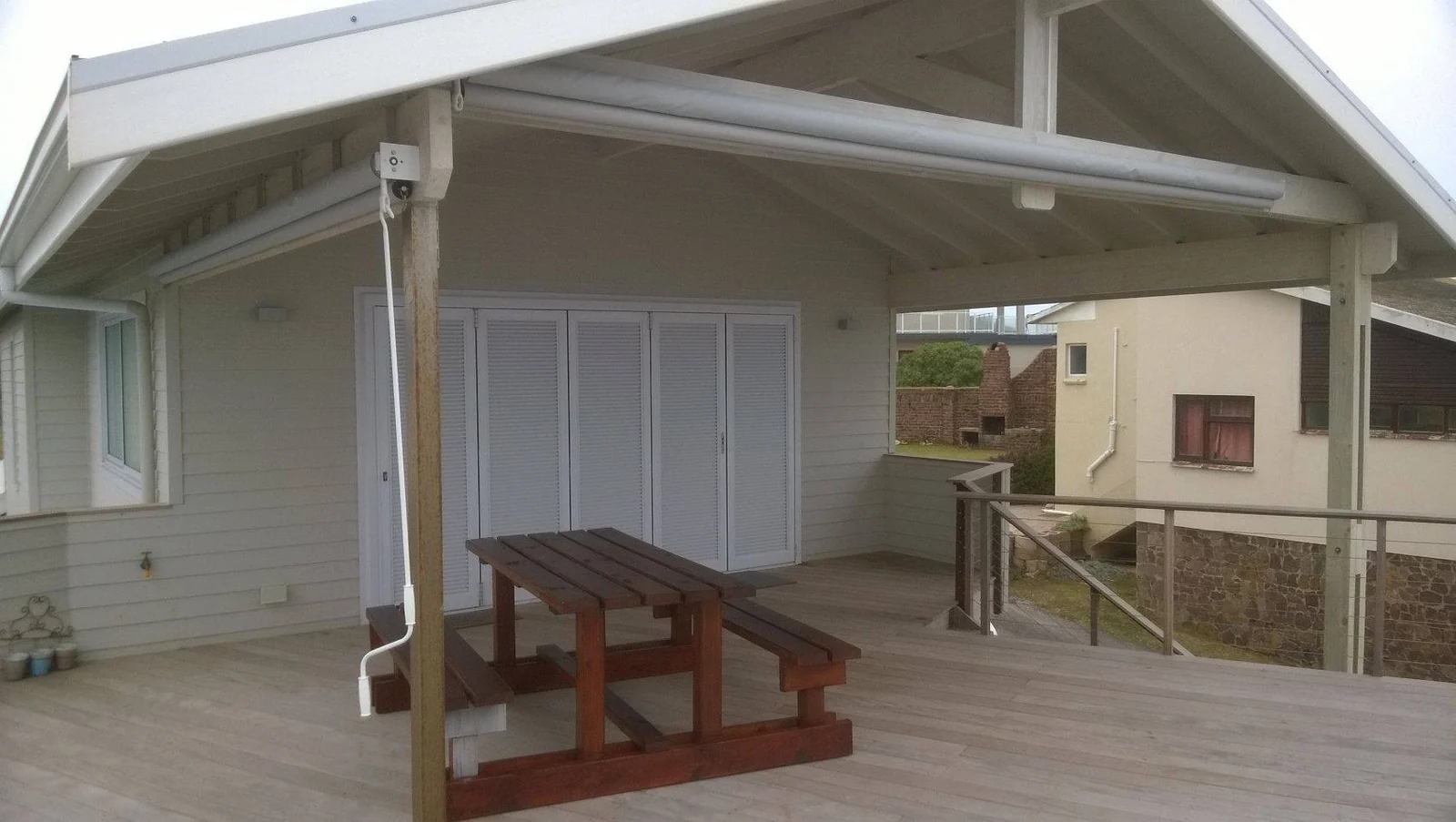 A covered timber deck with a retracted folding-arm awning at the gable end and a picnic table below, by Custom Blinds Shutters & Awnings, Garden Route, South Africa