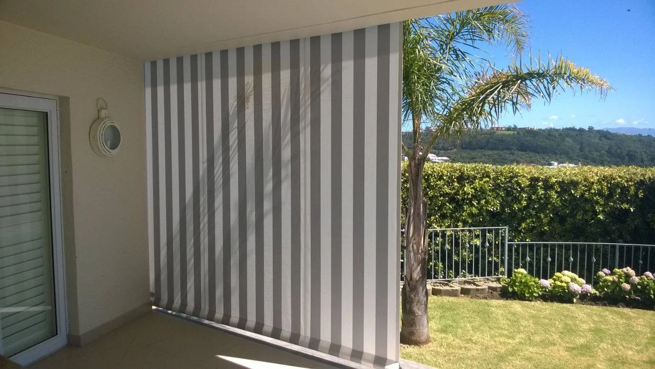 A grey and white striped outdoor blind lowered down the side of a covered patio in Knysna, by Custom Blinds Shutters & Awnings