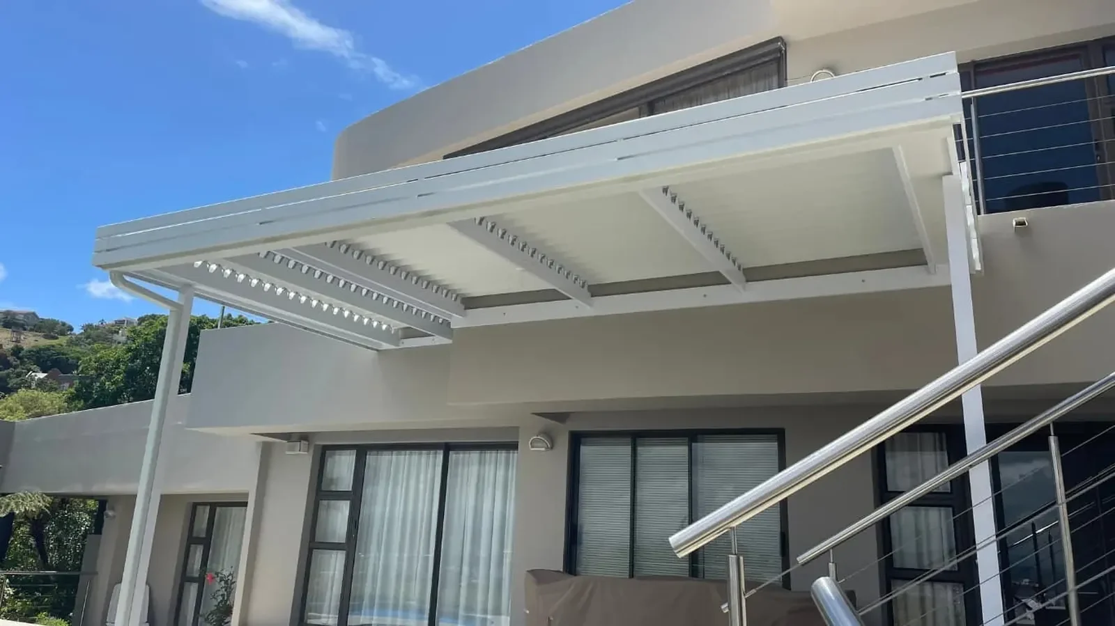 White louvred awnings Knysna Heads shade the patio, whilst steps with metal railings lead to the airy, sun-filled entrance. by Custom Blinds Shutters & Awnings, The Heads, Knysna, Garden Route, South Africa