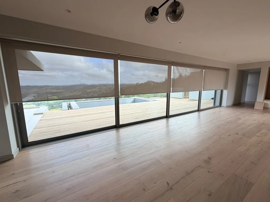 Living room sheer roller blinds lowered across a glass wall with a deck, pool and lagoon view, by Custom Blinds Shutters & Awnings, Simola Golf Estate, Knysna