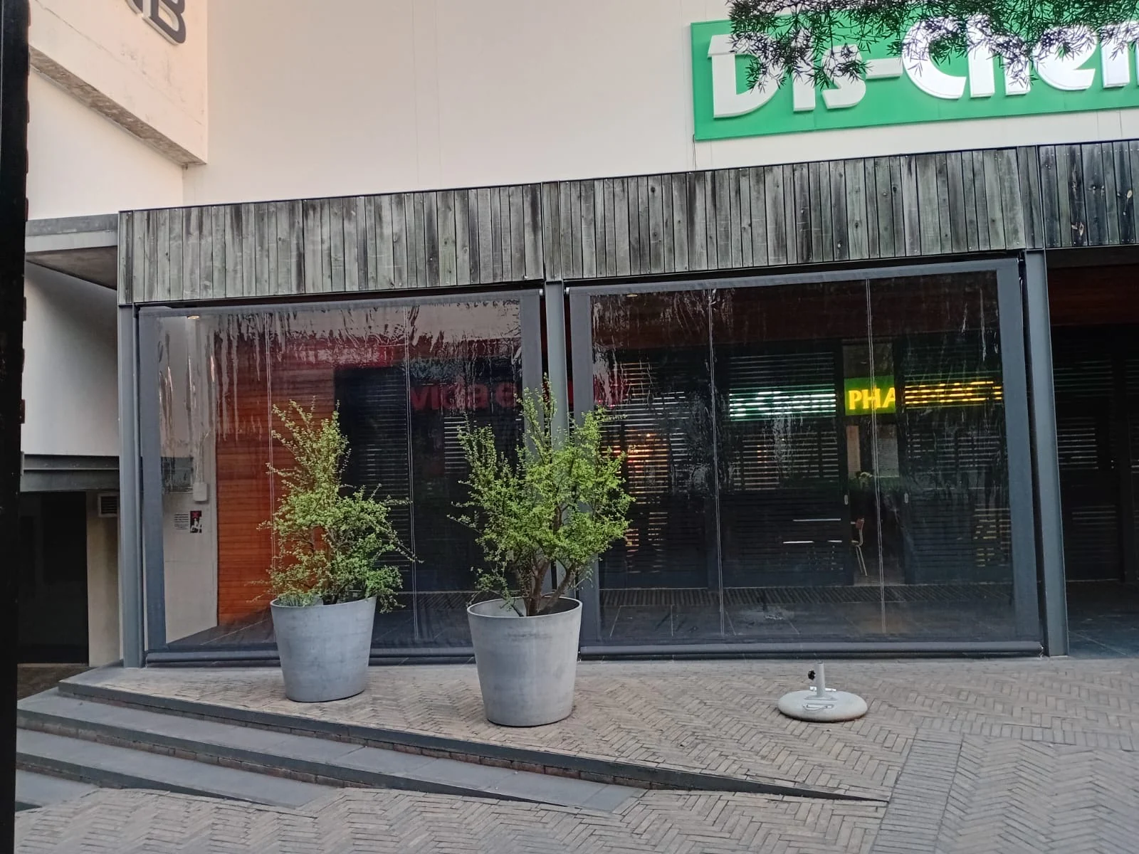 Exterior view of clear PVC blinds at Vida e Café Knysna Mall with Dis-Chem signage visible above, showing full weather enclosure of the outdoor seating terrace by Custom Blinds Shutters & Awnings, Garden Route, South Africa