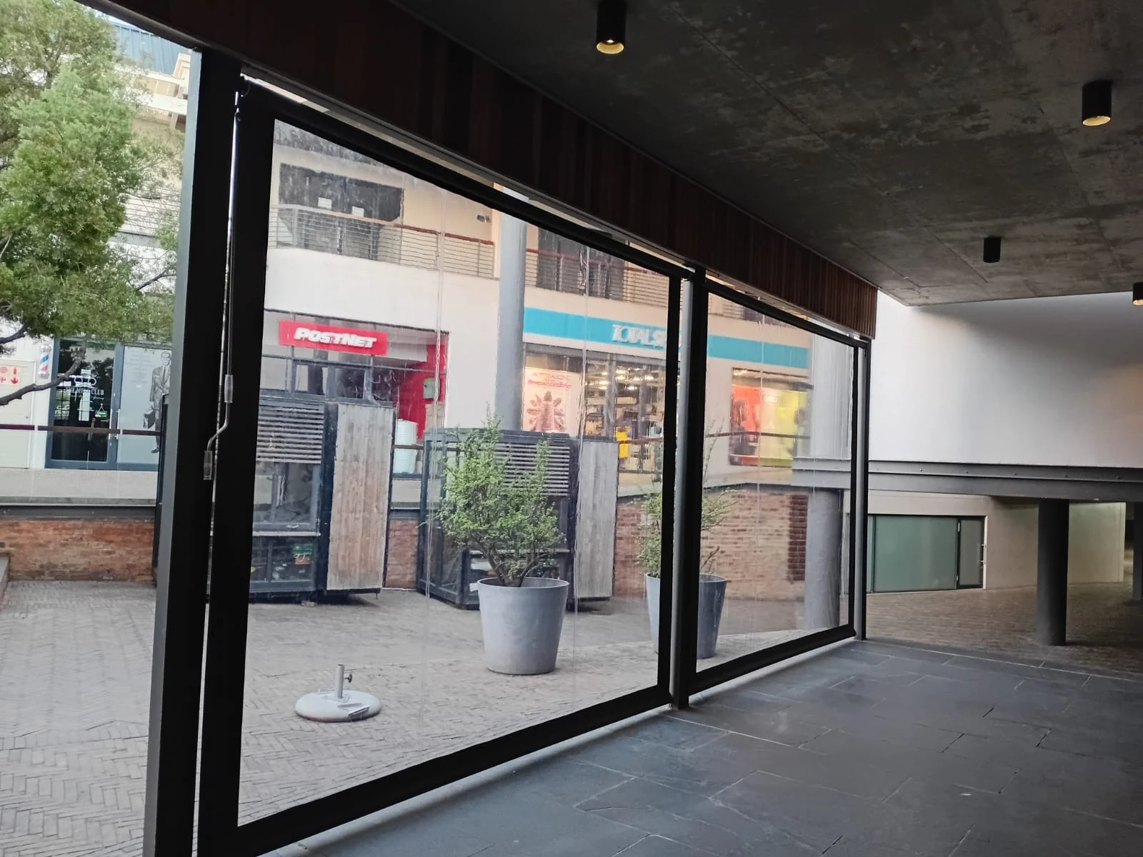 Clear PVC outdoor blinds installed at Vida e Café Knysna Mall, interior view showing PostNet and retail tenants visible through clear panels by Custom Blinds Shutters & Awnings, Garden Route, South Africa