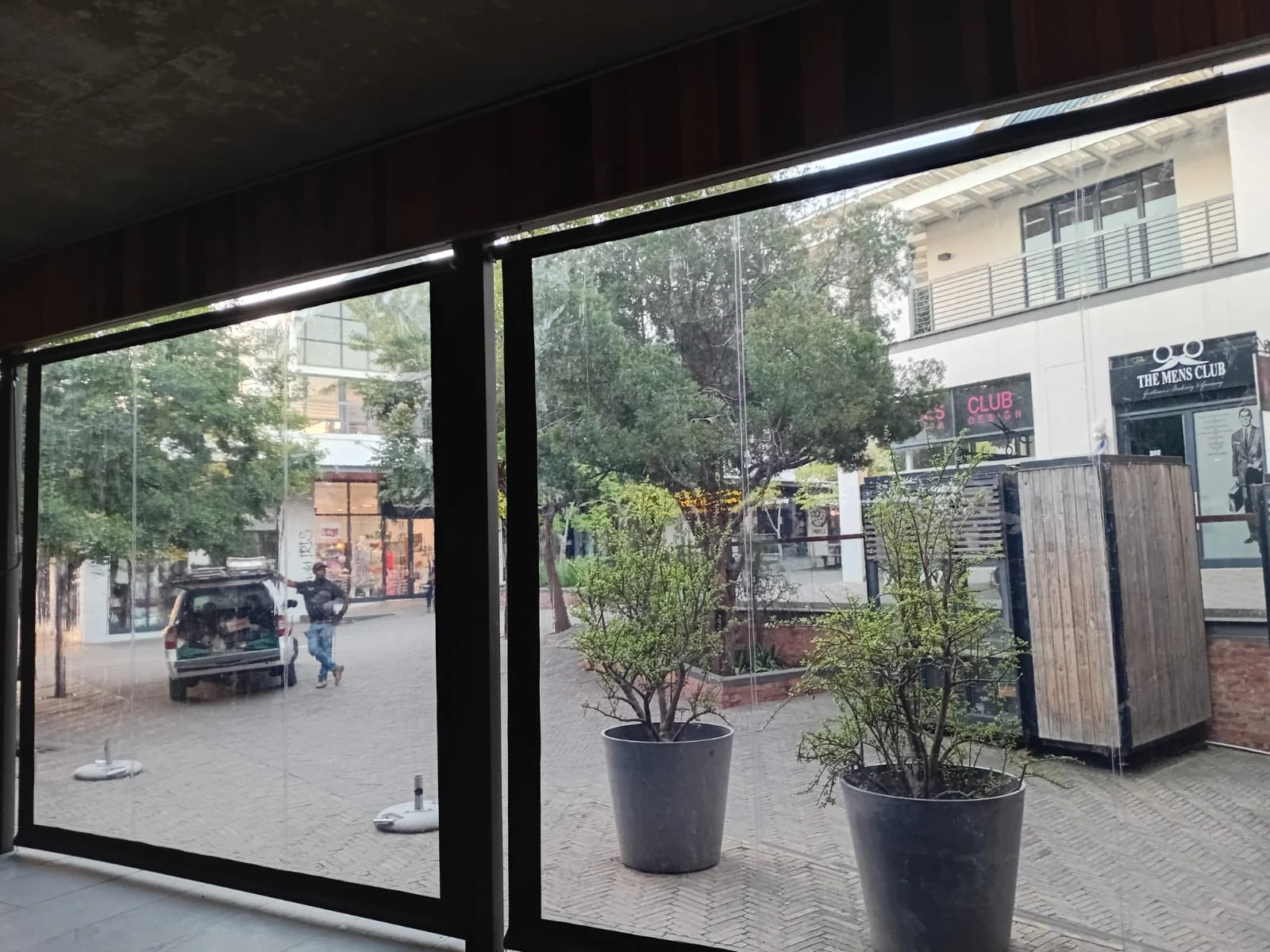 Clear PVC outdoor blinds at Vida e Café Knysna Mall, showing mall walkway and The Mens Club store visible from inside the enclosed seating area by Custom Blinds Shutters & Awnings, Garden Route, South Africa