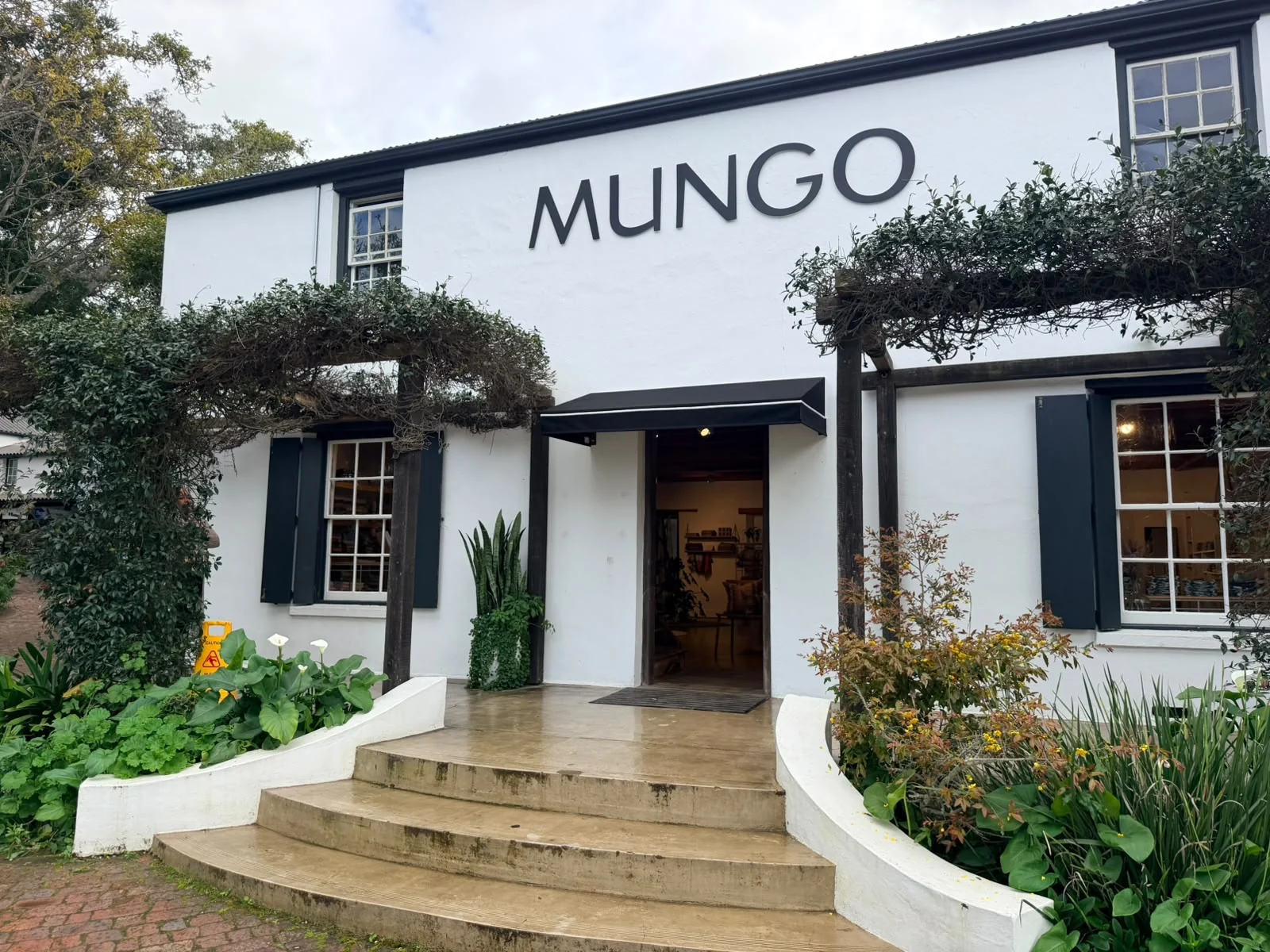 A black wedge awning fitted above the entrance door of the Mungo shopfront, below the sign, by Custom Blinds Shutters & Awnings, Plettenberg Bay, Garden Route, South Africa