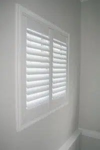 Custom Blinds South Africa Closed white plantation shutters on a small window in a light grey wall offer privacy and keep harsh sunlight out of your lounge. Knysna Garden Route & Online
