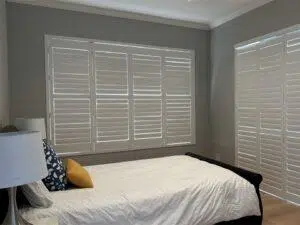Custom Blinds South Africa A sunny bedroom with grey walls, neat white window shutters, a cosy bed, and colourful pillows for a fresh, relaxing home feel. George Garden Route & Online