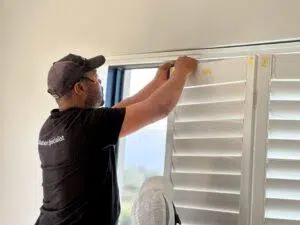 Custom Blinds South Africa Our Custom Blinds installer in a black cap and shirt fits white shutters indoors, bringing privacy and style into a sunny South African home. George Garden Route & Online