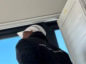 Custom Blinds South Africa a Custom Blinds installer in a white cap and dark hoodie stands by a wide window and open door, enjoying fresh air and clear views into the bright day. Garden Route & Online