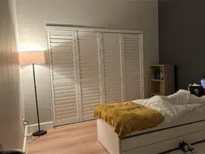 Custom Blinds South Africa A warm bedroom with timber floors, white bedding, bookshelves, and smart shuttered wardrobes brightening up the space. George Garden Route & Online